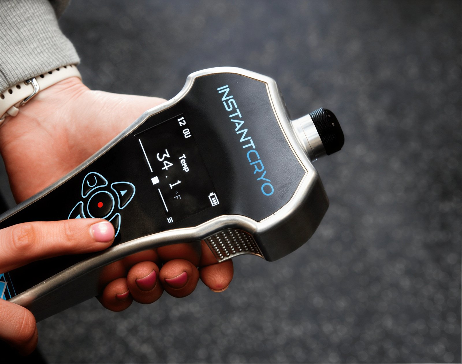 A silver cryotherapy device in a person's hand with the screen turned on.